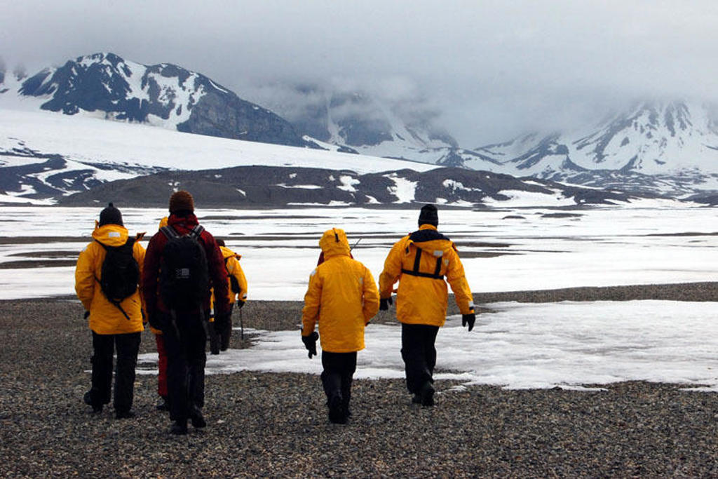 Wandelaars in gele jassen trekken door het besneeuwde landschap van Spitsbergen, met bergen op de achtergrond.