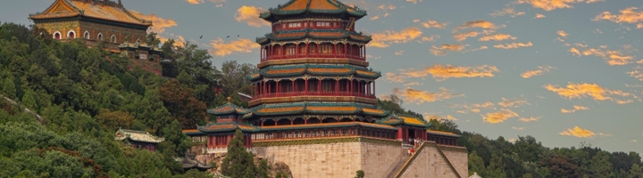 Zomerpaleis in Beijing met traditionele paviljoens op een groene heuvel bij zonsondergang.