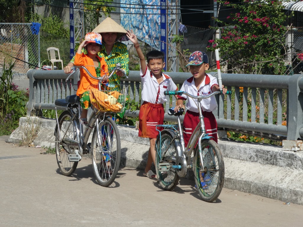 Kinderen met fietsen en een vrouw met conische hoed langs de weg tijdens een fietsvakantie in Vietnam.