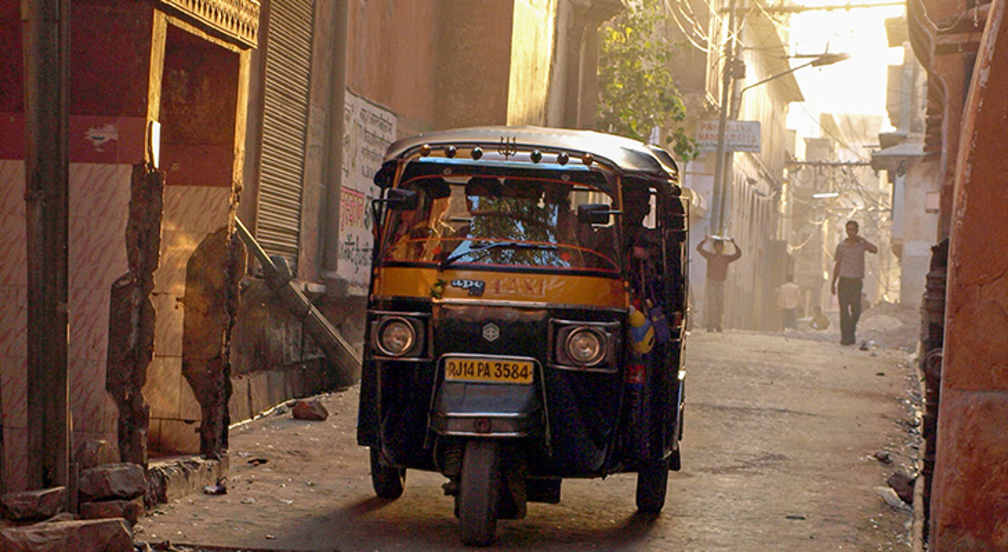 Tuk tuk in de straten van India Tuk-tuk in een smalle straat met ochtendlicht en voorbijgangers op de achtergrond.
