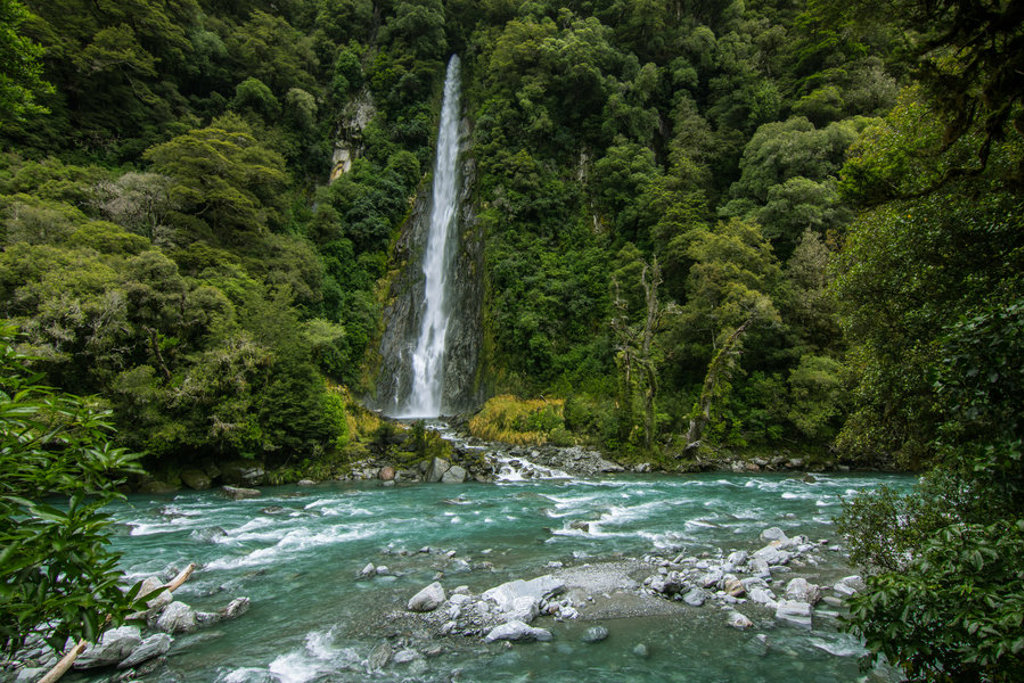 Waterval in een groen regenwoud bij een helderblauwe rivier in Nieuw-Zeeland tijdens groepsrondreis Australië & Nieuw-Zeeland.