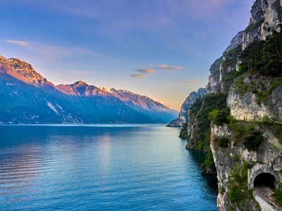 Uitzicht op het Gardameer met bergketen en rotswand met tunnel langs de oever in Italië.