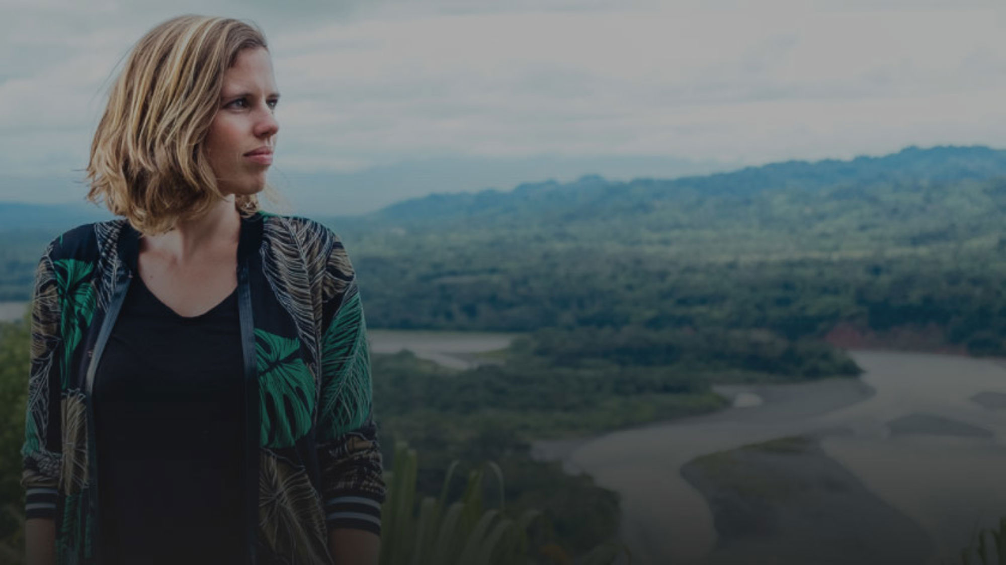 Amazone, Sandra Korstjens Vrouw kijkt uit over een groene vallei met rivier en bergen op de achtergrond.