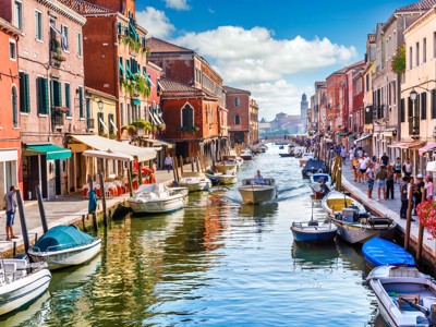 Kanaal in Venetië met kleurrijke gevels, terrasjes en boten langs de kade.