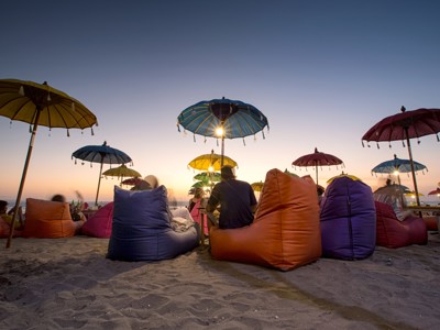 Zonsondergang op het strand van Bali met kleurrijke parasols en zitzakken.