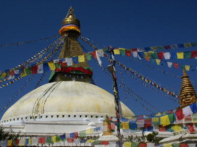 Boudhanath-stoepa in Kathmandu met gebedsvlaggen tegen een helderblauwe lucht.
