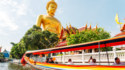 Gouden Boeddhabeeld bij een Thaise tempel, gezien vanaf een longtailboot op het water.