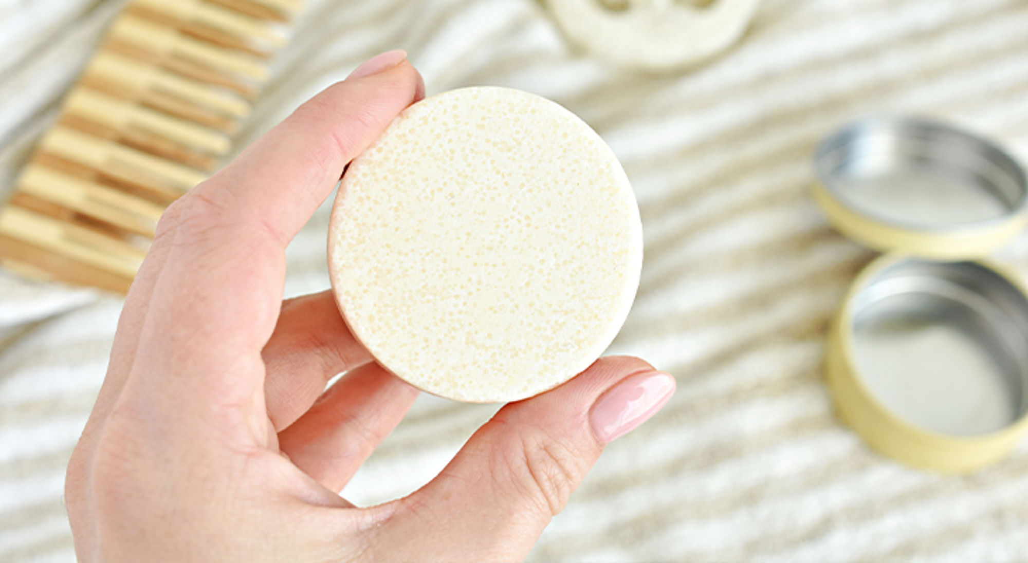 Cadeau voor reiziger zero waste zeep Hand houdt een ronde shampoo bar vast, met zeepbakje op de achtergrond.
