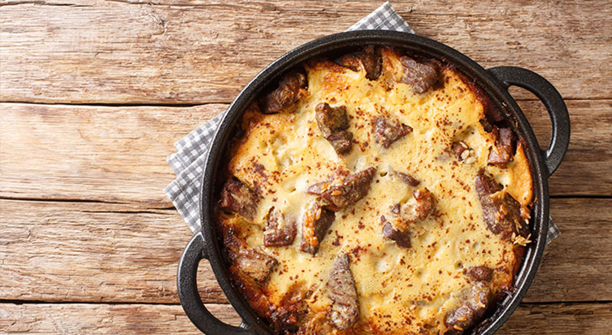 Albanese keuken Ovenschotel met aardappelschijfjes en vlees in een gietijzeren pan op een houten tafel.