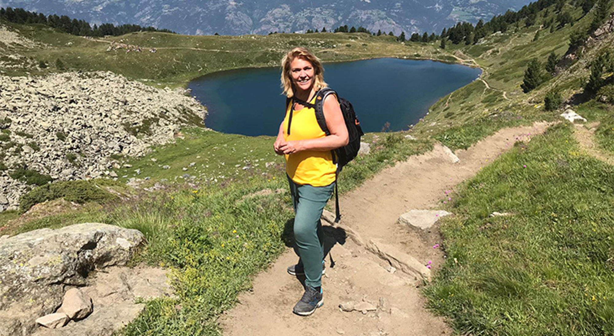 Annemieke Wandelaar met rugzak op bergpad met uitzicht op alpien bergmeer.