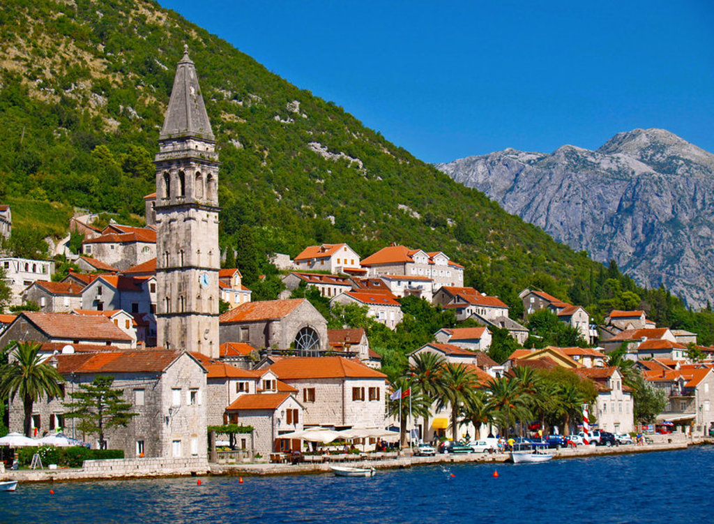 Kustplaats Perast aan de Baai van Kotor met kerktoren, rode daken en bergen op de achtergrond.