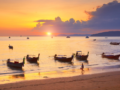 Zonsondergang bij Krabi met longtailboten voor de kust en wandelaars op het strand.