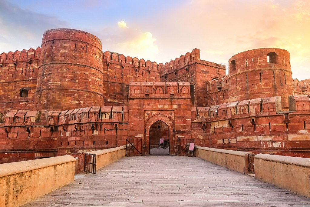 Rode fortmuur met toegangspoort en brug bij Agra Fort in India tijdens zonsondergang.