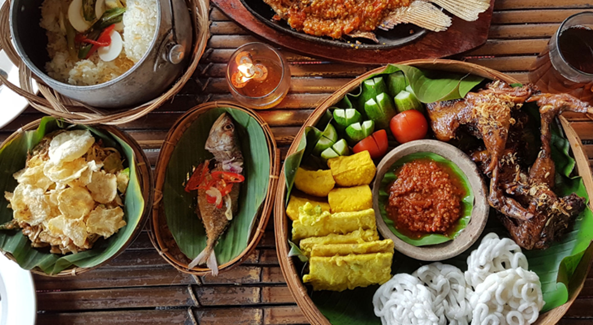 Indonesische rijsttafel met gegrilde kip, vis, groenten, tofu en sambal op bananenblad.