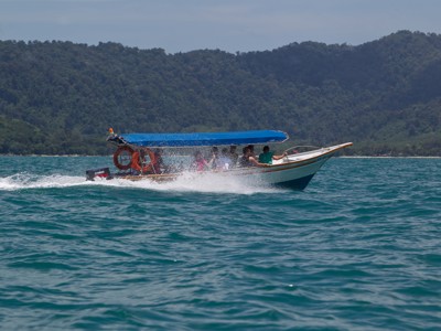 Speedboot met passagiers op zee langs een groen, bergachtig eiland in Maleisië.