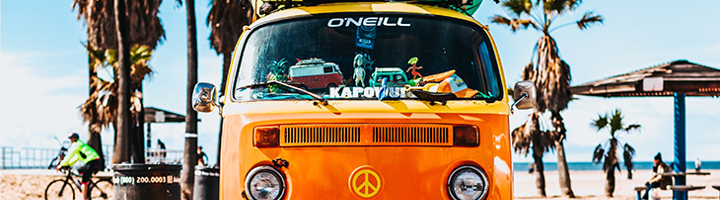 Oranje camperbus met surfboards op het dak aan het strand, passend bij YouTube reistips voor Australië en Nieuw-Zeeland.