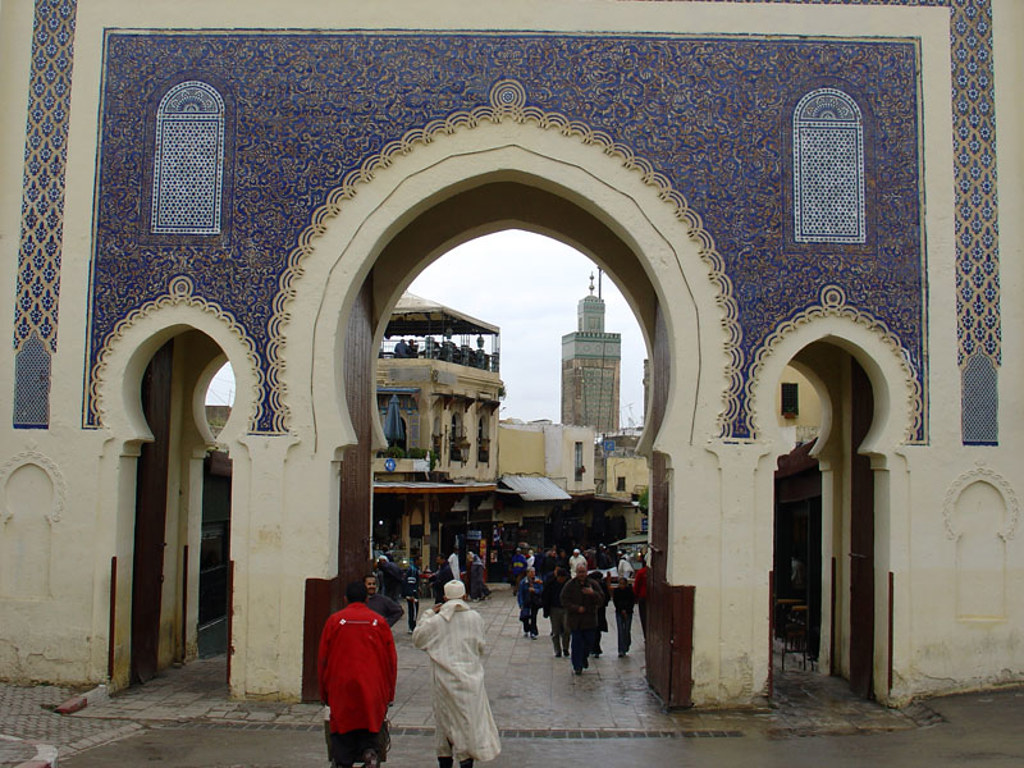 Poort met blauw mozaïek bij de medina van Fez, met marktstraat en minaret op de achtergrond.