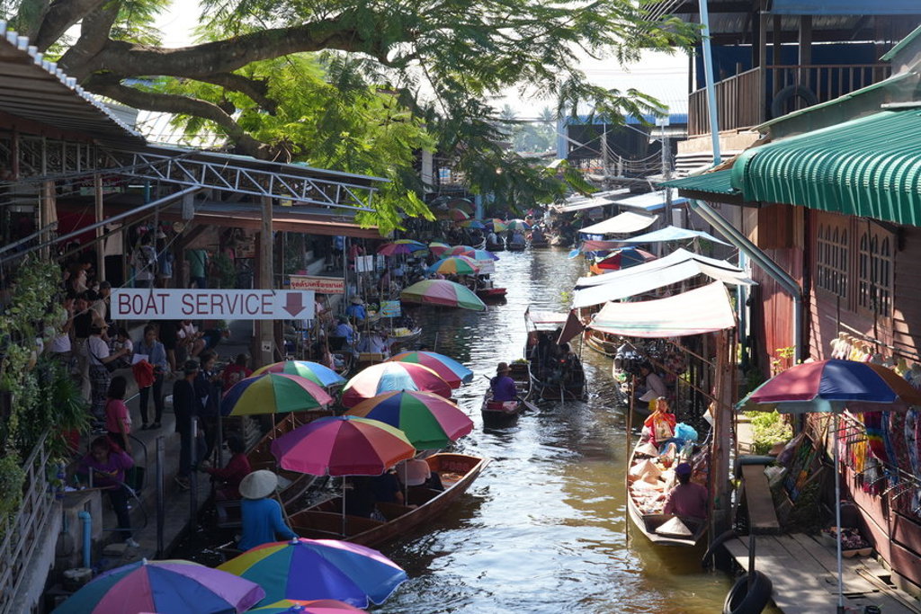 Drijvende markt in Thailand met boten en kleurrijke parasols langs een smal kanaal.