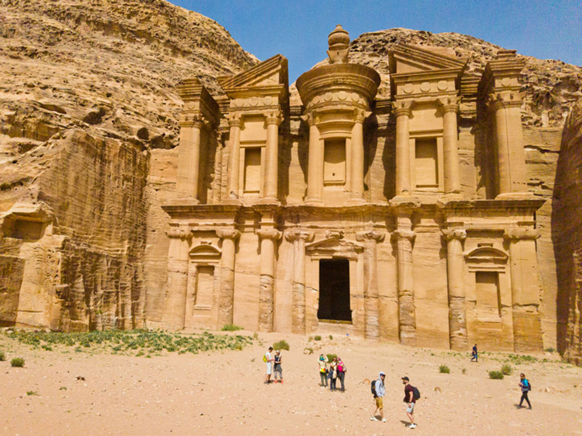 De rotsuitgehouwen gevel van Ad Deir (het Klooster) in Petra, Jordanië, met bezoekers op het plein.