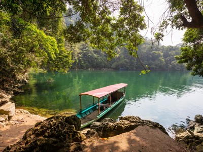 Boot aan de oever van een groen meer, omringd door jungle, tijdens de Route China & Vietnam 20 dagen.