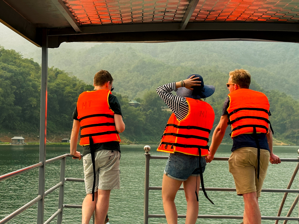Jonge reizigers in reddingsvesten op een boot, met uitzicht op het groene berglandschap in Vietnam.