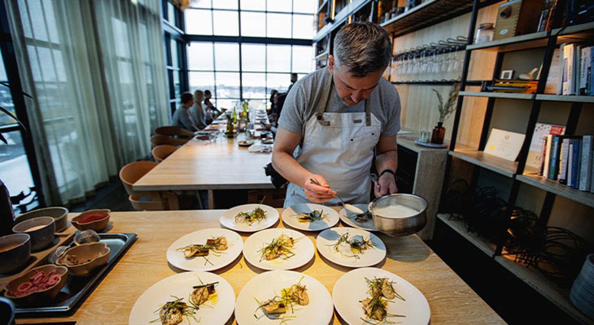 Keuken Estland Chef maakt borden op in een modern restaurant met lange tafel en uitzicht door grote ramen.