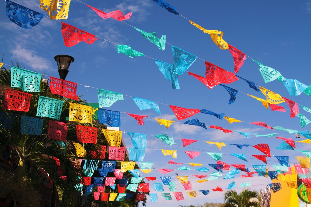 Gekleurde papel picado vlaggetjes boven een straat in Mexico tijdens familiereis langs hoogtepunten.