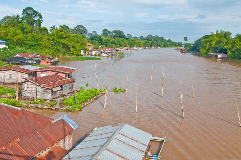 Rivierlandschap in Thailand met houten huizen langs de oever, omringd door groen.