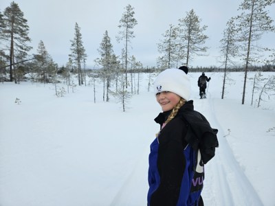 Kind draait zich om tijdens sneeuwschoenwandeling door het winterse landschap van Lapland.