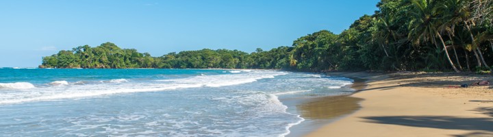 Zandstrand van Punta Uva in Costa Rica met palmbomen, tropisch groen en golven aan de kust.