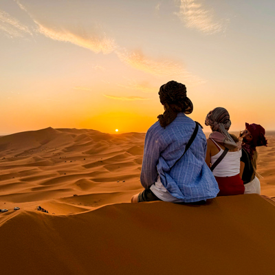 Gezin met lokale gids kijkt uit over de Sahara-duinen bij zonsondergang tijdens een familiereis in Marokko.