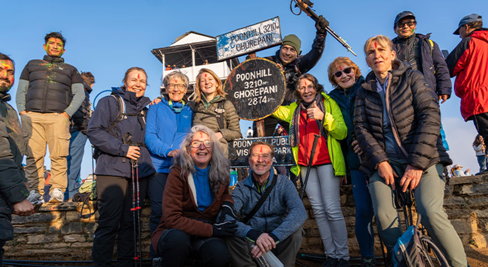 Groep wandelaars poseert bij het Poon Hill-bord (3210 m) in Nepal tijdens een trekking.