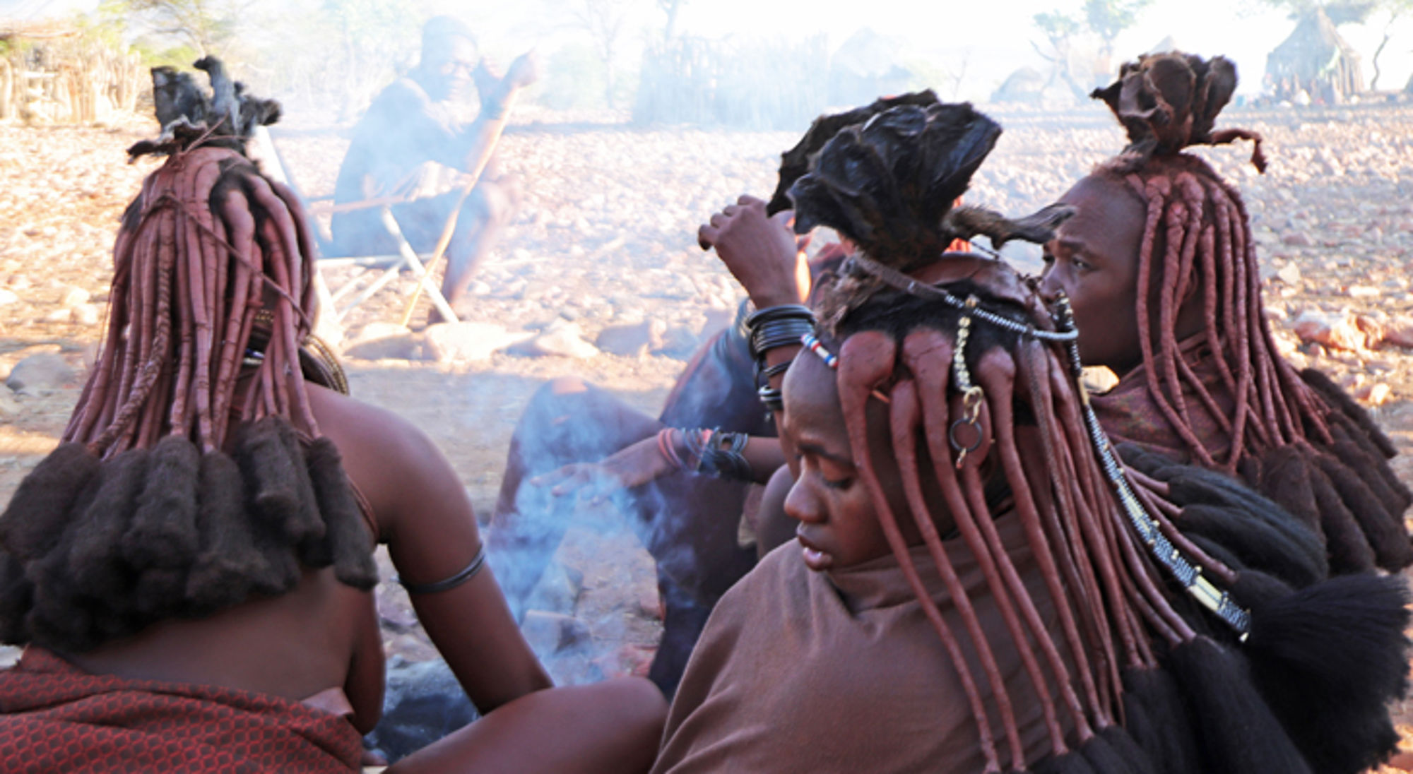 ontmoeting met locals in een Himba dorp Vrouwen met traditionele kapsels en sieraden zitten rond een kampvuur in een dorp.
