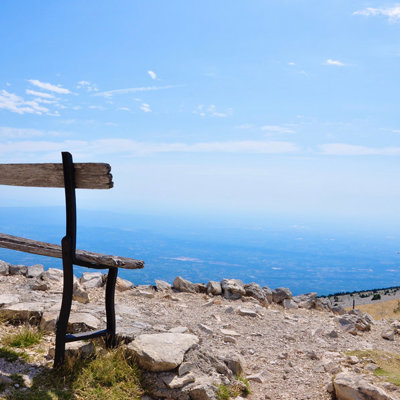 Houten bankje op de top van de Mont Ventoux met uitzicht over de Provence onder een blauwe lucht.