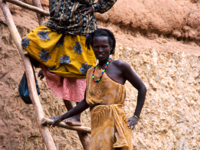 Twee vrouwen in traditionele kleding op een houten ladder tegen een rotswand in Ethiopië.