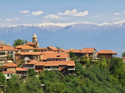 Uitzicht op het Georgische stadje Sighnaghi met rode daken en kerktoren, met besneeuwde Kaukasus op de achtergrond.