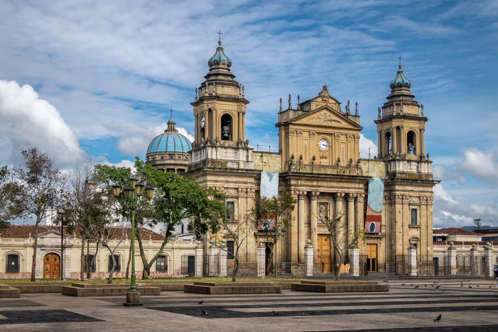 Kathedraal van Guatemala-Stad met koepel en klokkentorens aan een groot plein onder een blauwe lucht.