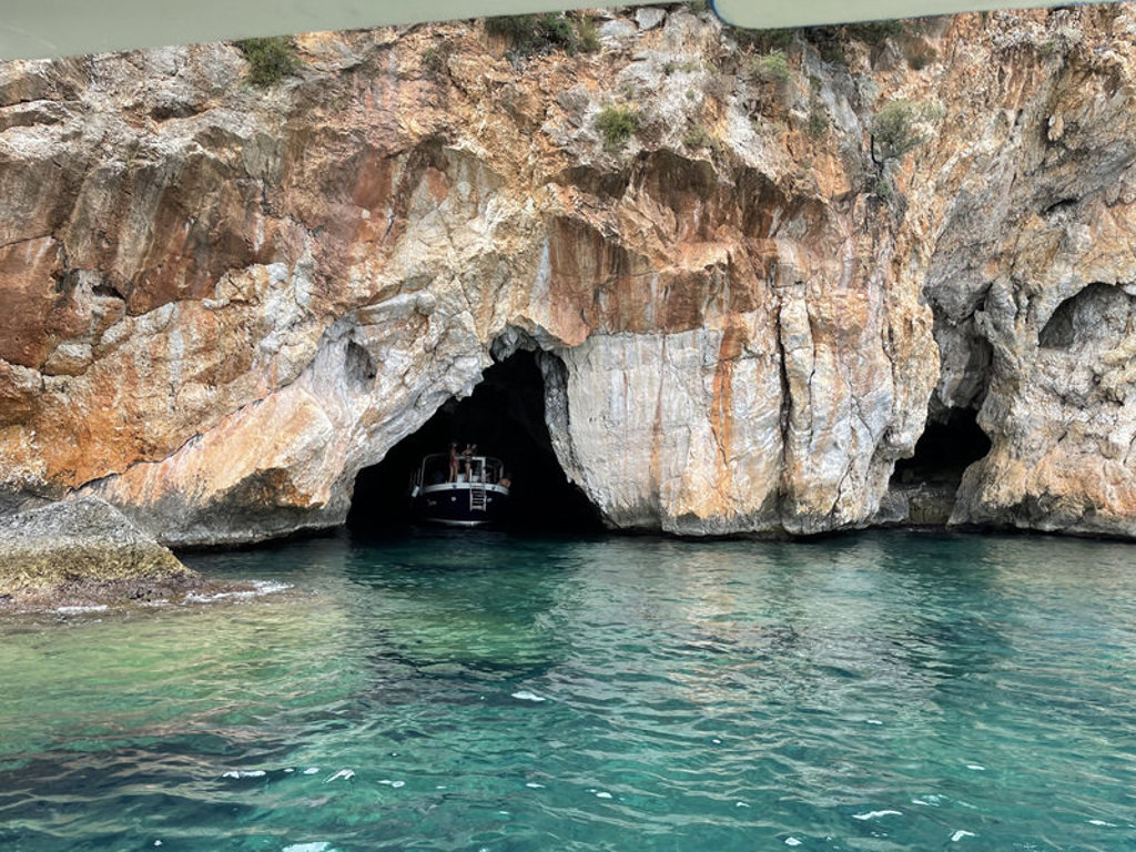 Boot vaart een zeegrot in bij de rotsachtige kust van Zuid-Italië, met helder turquoise water.