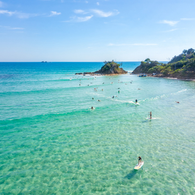 Surfers tijdens een ochtend surfles in de baai van Byron Bay, met helderblauw water en groene kustlijn.