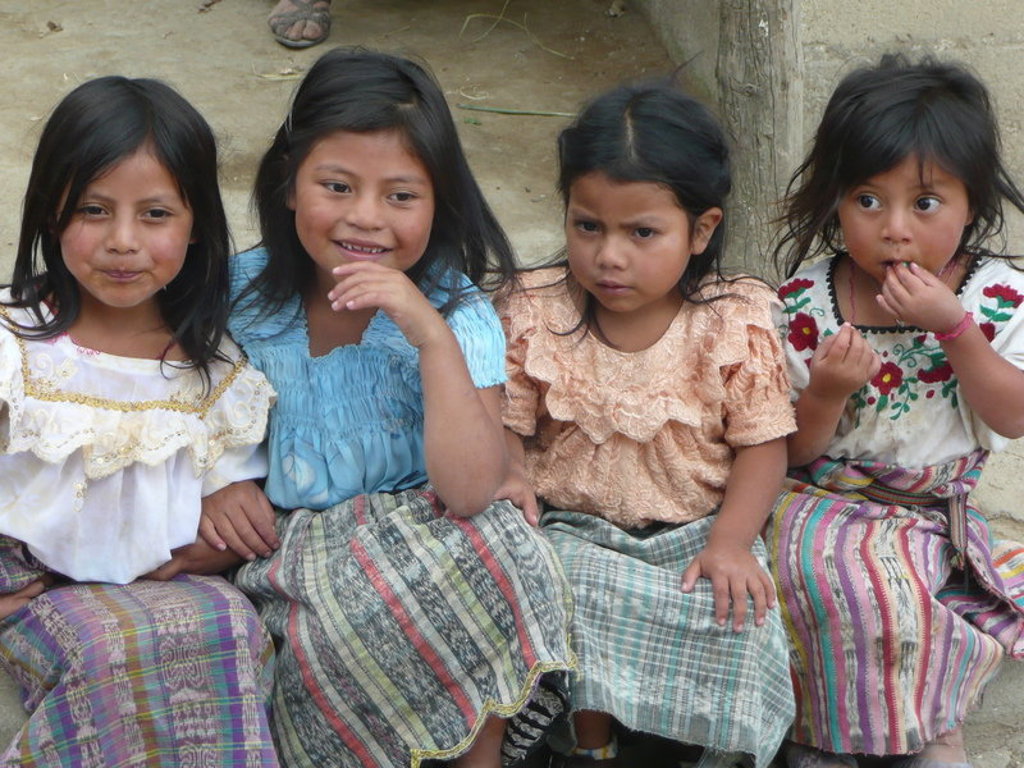 Vier meisjes in traditionele kleding zitten naast elkaar in Guatemala tijdens een groepsrondreis.