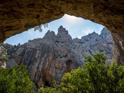 Uitzicht vanuit een grot op steile rotswanden en groene begroeiing tijdens de wandelvakantie op Sardinië.