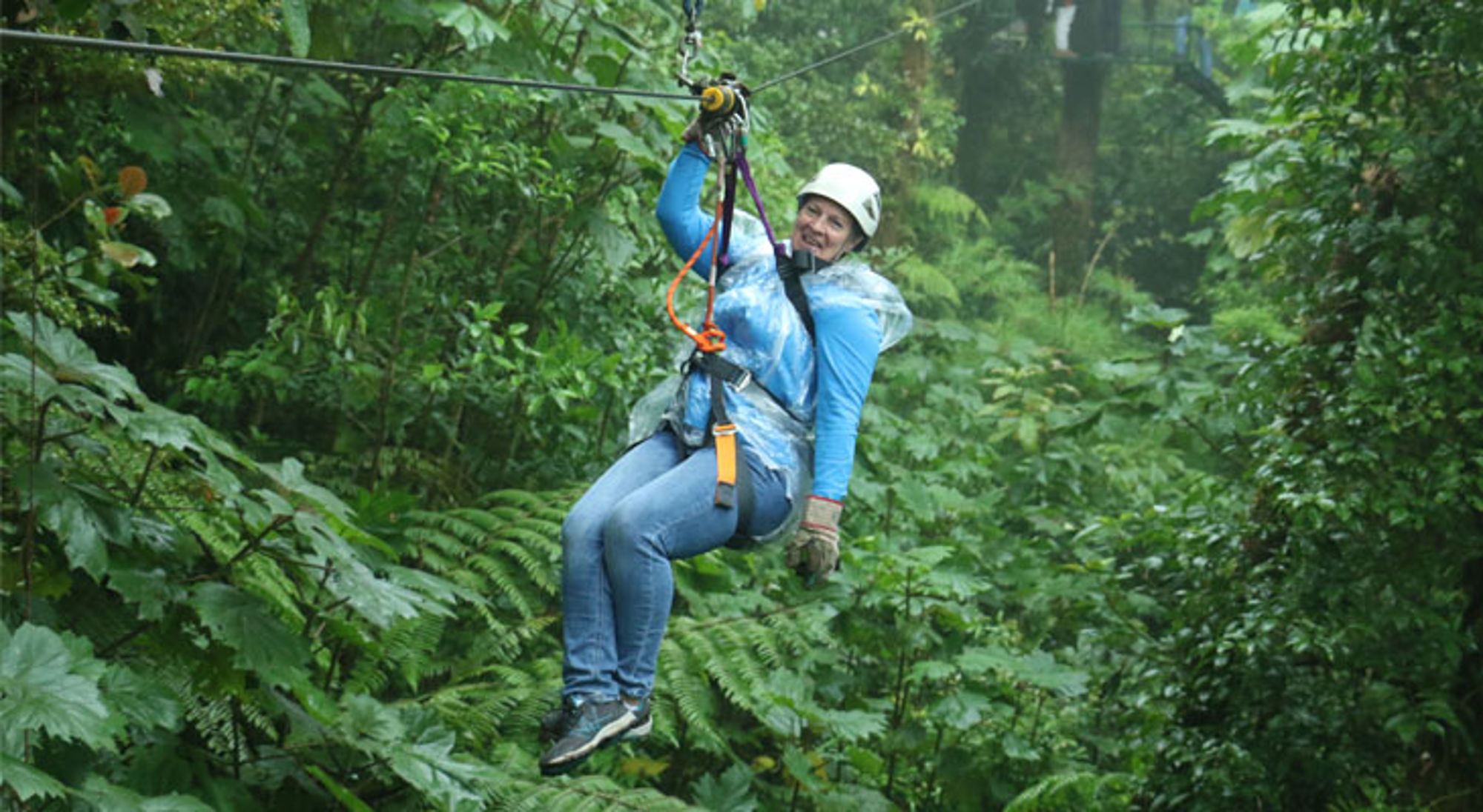 Vrouw aan zipline door dicht regenwoud, met helm en harnas.