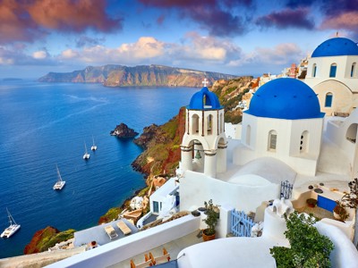 Blauw-witte kerkkoepels in Oia op Santorini met uitzicht op de caldera en zeilboten in zee.