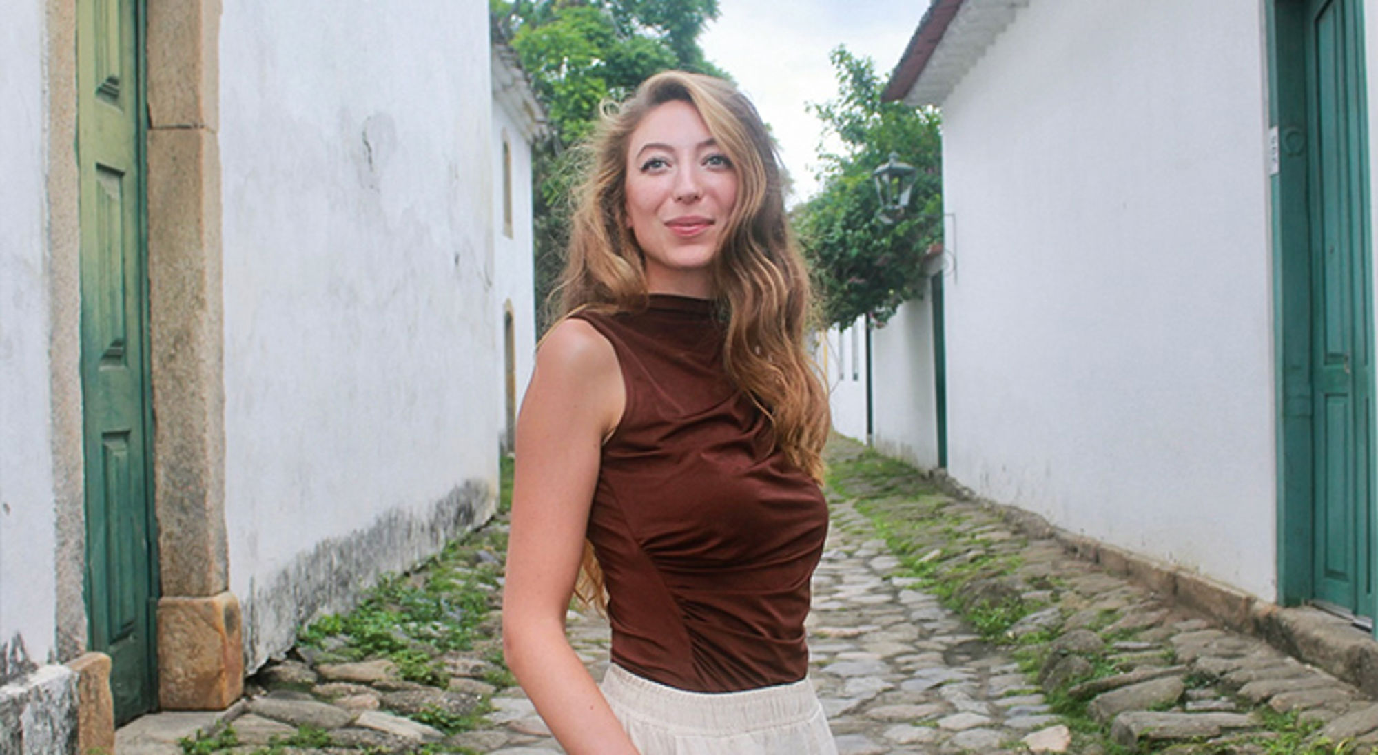 Laura in Brazilië Vrouw poseert in een smal straatje met witte huizen en groene deuren.