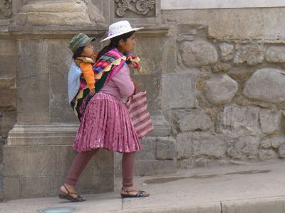 Vrouw in traditionele kleding draagt een kind op haar rug in Peru tijdens de route Argentinië, Bolivia en Peru.