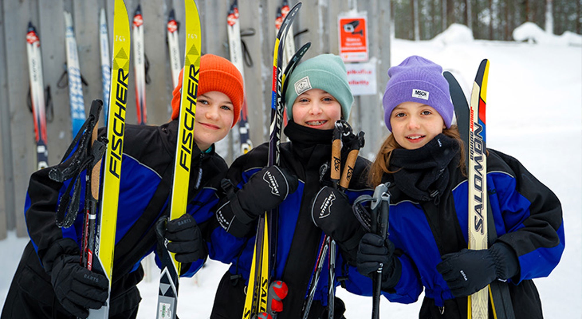 Familiereis Fins Lapland Drie kinderen in winterkleding met langlaufski’s en skistokken in een besneeuwd landschap.