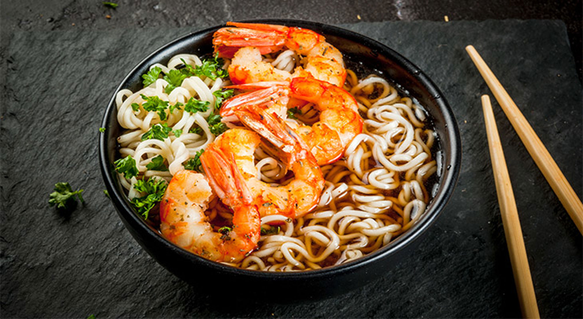 Ramen met garnalen in Japan Kom noedelsoep met garnalen en verse kruiden, met eetstokjes ernaast.