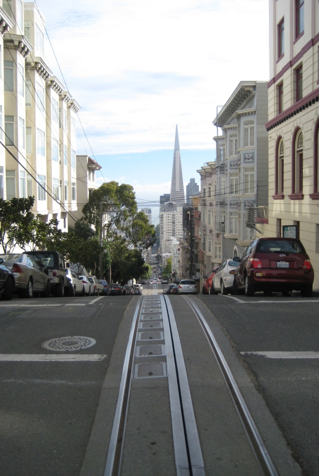 Kabelspoorrails in een steile straat in San Francisco met de Transamerica Pyramid op de achtergrond.