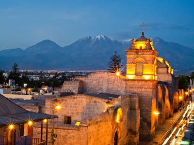 Verlichte kathedraal in Arequipa bij schemering, met de besneeuwde vulkaan El Misti op de achtergrond.