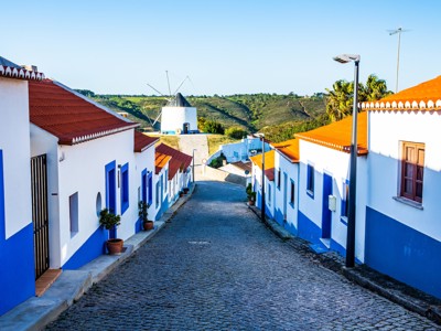 Straat met wit-blauwe huizen en windmolen in een dorp in de Alentejo, Portugal.